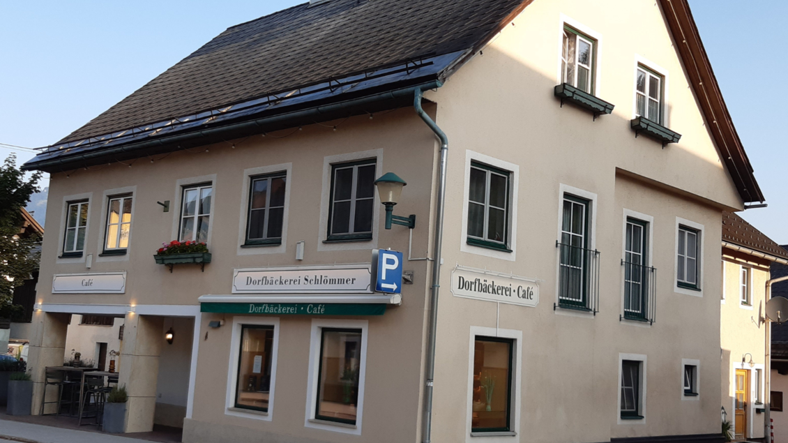 Ein helles Gebäude mit einem Café und einer Bäckerei. Die Fassade ist freundlich und einladend, mit Pflanzen an den Fenstern. | © Daniela Casari