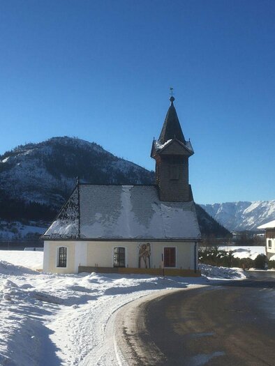 A picturesque church in a snowy landscape. In the background, mountains and a blue sky are visible.