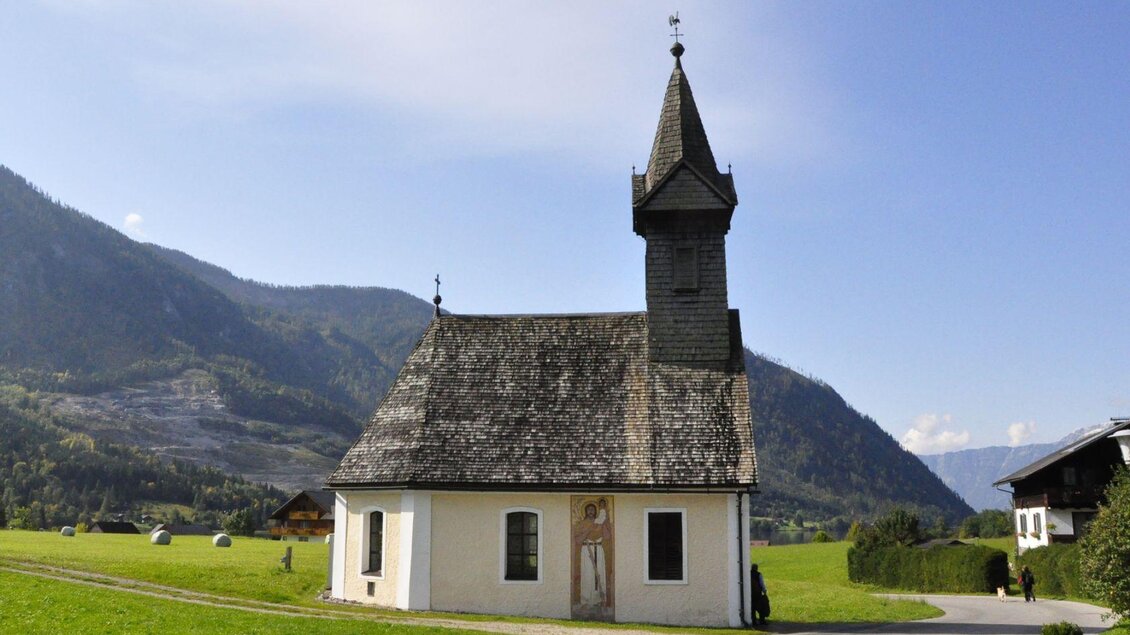Eine kleine, charmante Kirche mit einem hohen Turm. Sie liegt malerisch in einer grünen Landschaft vor den Bergen. | © TVB Ausseerland - Salzkammergut/Franz Steinegger