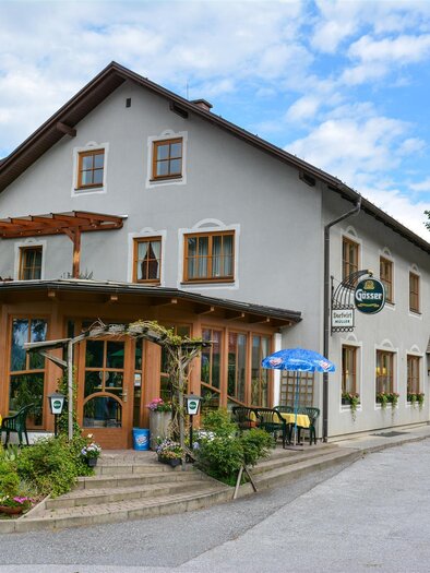 Ein charmantes Gebäude mit einem Restaurant und einem gemütlichen Außenbereich. Umgeben von Bäumen und einer kleinen Straße. | © Dorfwirt Müller