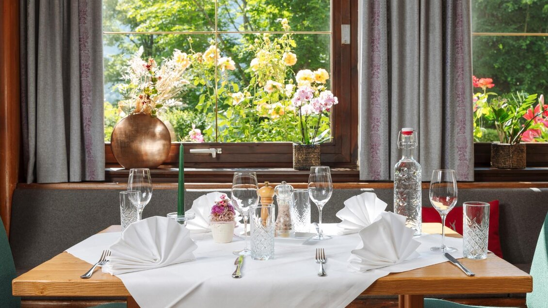 Ein elegant gedeckter Tisch mit gläsernem Geschirr und gefalteten Servietten. Im Hintergrund sind blühende Pflanzen und viel Grün sichtbar. | © Gasthaus Stöckl