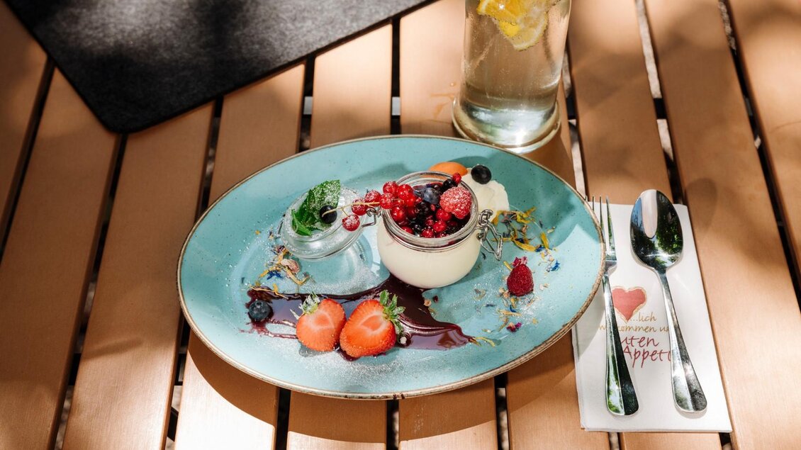 Ein elegantes Dessert auf einem blauen Teller, garniert mit frischen Beeren und Minze. Daneben steht eine Flasche mit limonadigem Wasser. | © Gasthaus Stöckl