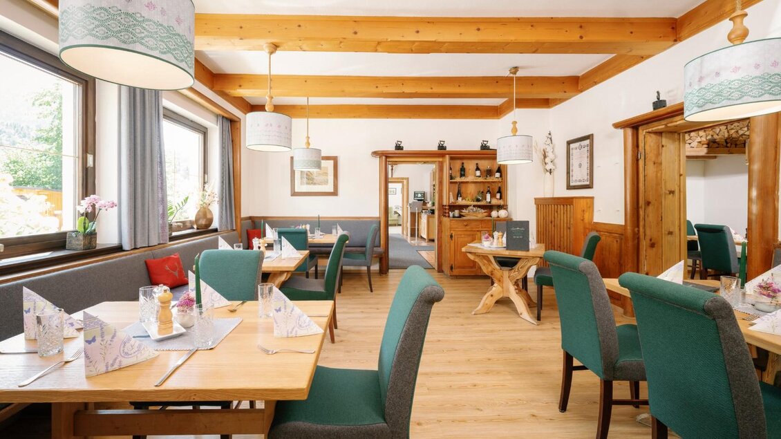 Ein gemütlicher Gastraum mit Holzmöbeln und grünen Stühlen. Große Fenster sorgen für viel Tageslicht und eine einladende Atmosphäre. | © Gasthaus Stöckl
