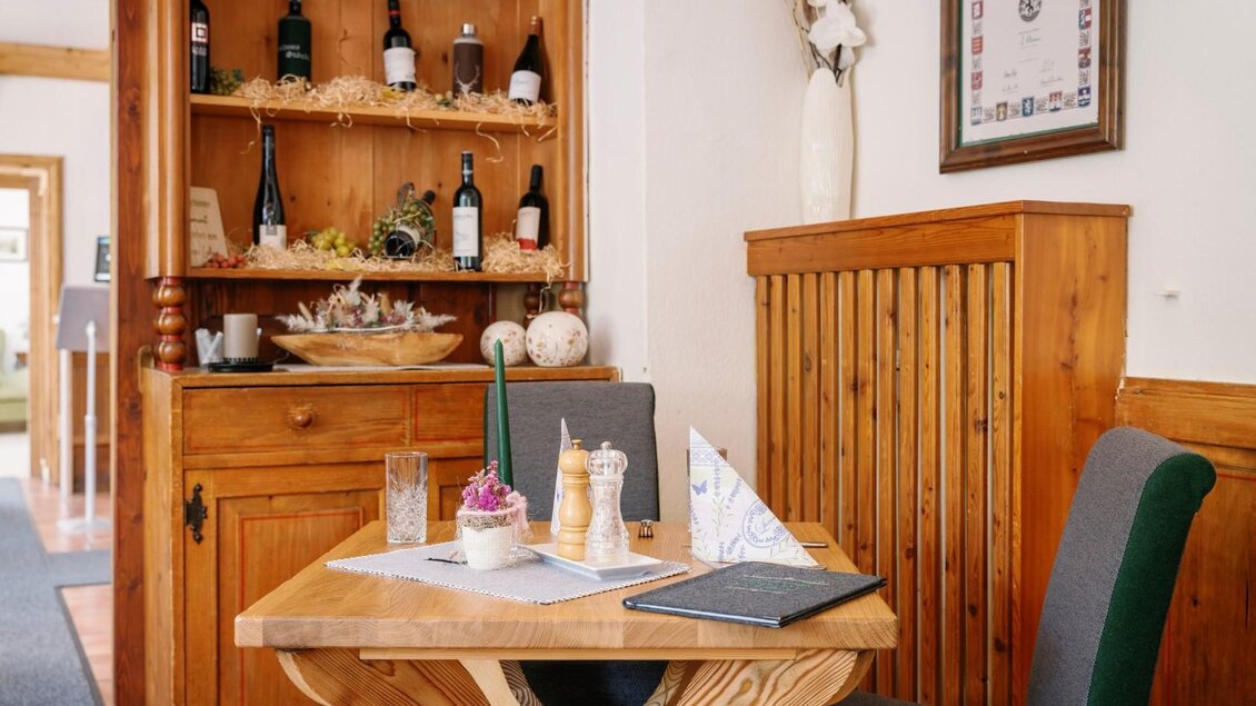 Ein gemütlicher Tisch in einem Restaurant mit Holzregalen im Hintergrund. Auf dem Tisch stehen Speisekarten und Dekoration, die eine einladende Atmosphäre schaffen. | © Gasthaus Stöckl