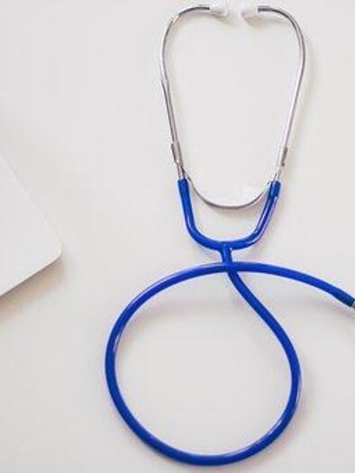 A stethoscope lies next to a laptop on a table. The stethoscope has a blue tube and is often used in medicine. | © Symbolfoto