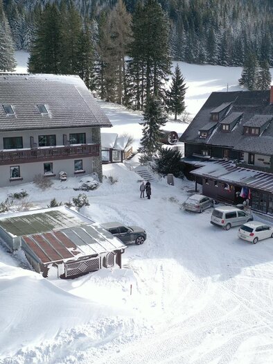 Ein schneebedecktes Landschaftsbild mit zwei Gebäuden. Autos parken auf dem verschneiten Parkplatz. | © Draxlerhaus