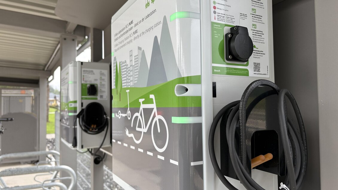 Eine Fahrradladestation mit zwei Ladegeräten und einer klaren Anleitung. Die Station befindet sich in einer modernen Umgebung mit Sicht auf Berge. | © TV Hochsteiermark