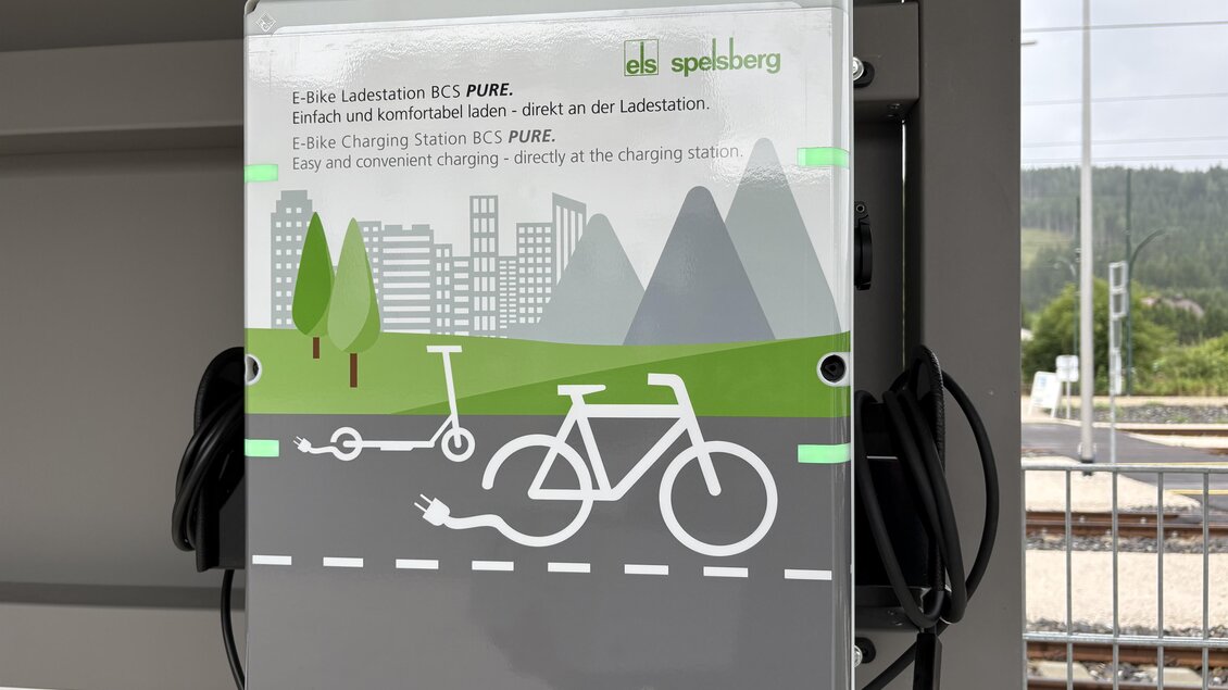 Eine Ladestation für Fahrräder und E-Scooter mit einer klaren Anleitung. Im Hintergrund sind Berge und eine Stadtansicht zu sehen. | © TV Hochsteiermark