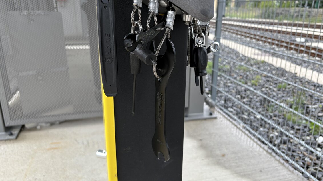 Ein Sichtgerät mit mehreren Schlüsselanhängern und einem Handschuh an der Seite. Im Hintergrund sind Gleise sichtbar. | © TV Hochsteiermark