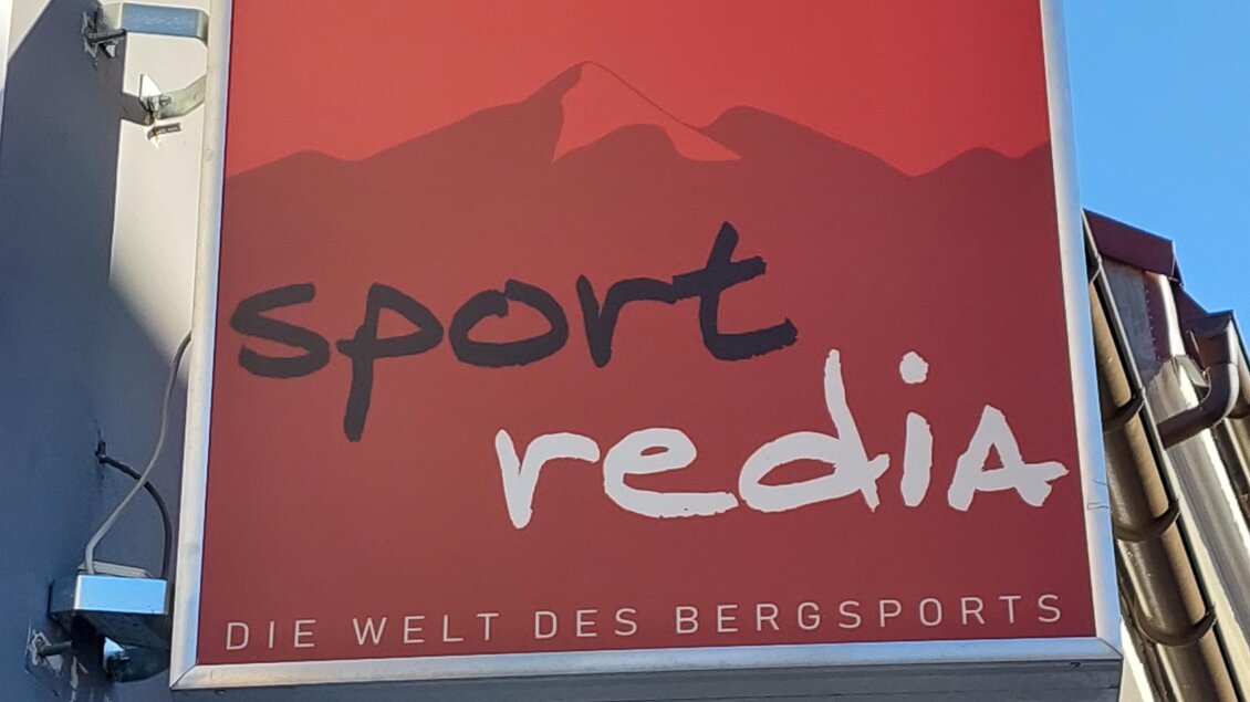 Ein Schild mit dem Schriftzug "sport redia" und der Unterzeile "DIE WELT DES BERGSPORTS". Im Hintergrund sind stilisierte Berge zu sehen. | © TV Hochsteiermark | Brigitte Digruber