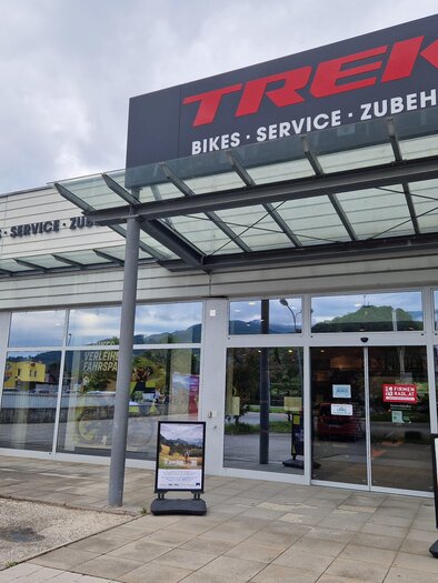 The image shows the entrance in the outdoor view of the TREK Bikestore in Bruck an der Mur. Bikes - Service - Accessories | © Zita Molnar Tengerdi