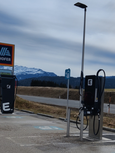 Ladestationen für Elektrofahrzeuge an einem Parkplatz. Im Hintergrund sind Berge und ein bewölkter Himmel zu sehen. | © TVB Ausseerland Salzkammergut (c) Michaela Schilcher