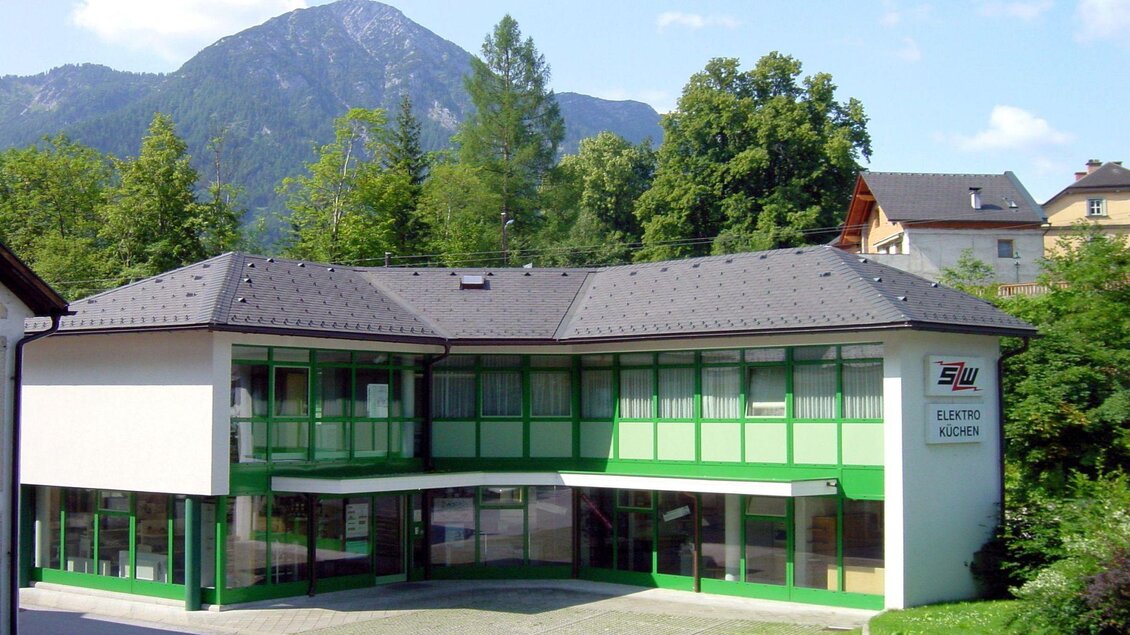 Ein modernes Bürogebäude mit grüner Fassade und großen Fenstern. Im Hintergrund sind Bäume und Berge sichtbar. | © Schwarz Wagendorffer