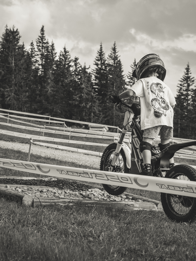 A boy rides a small motorcycle over an obstacle course. In the background, trees can be seen and the track is marked with barrier tape. | © (c) Trialstars / Josh Absenger