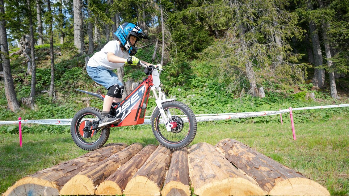 Ein Junge fährt mit einem Fahrrad über Baumstämme. Er trägt einen Helm und Handschuhe und sieht konzentriert aus. | © Trialstars - Andreas Pilz