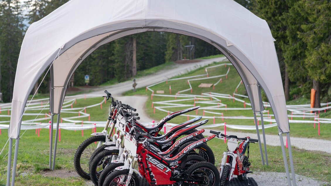 Eine Auswahl von Fahrrädern steht unter einem Pavillon. Im Hintergrund ist ein kurvenreicher Pfad in der Natur zu sehen. | © Trialstars - Andreas Pilz