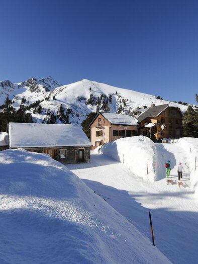 A picturesque mountain village in the snow with snow-covered huts. In the background, the majestic mountains and a clear blue sky can be seen. | © Erlebnisregion Murtal