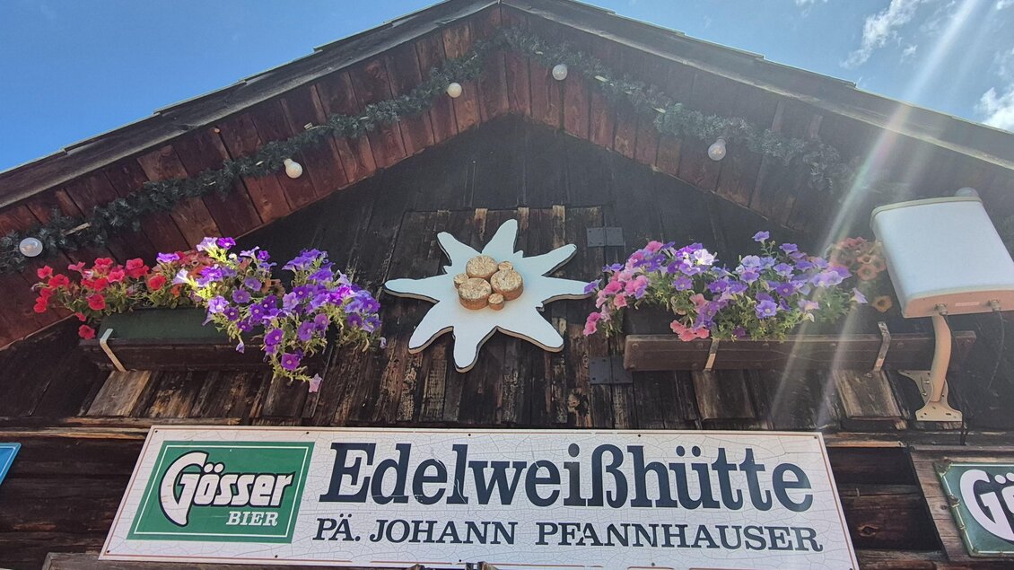 Ein traditionelles Holzhaus mit dem Schild "Edelweißhütte". Blumenkästen mit bunten Blumen zieren die Fassade. | © TV Hochsteiermark