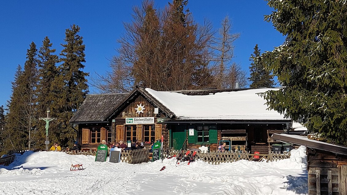 Eine gemütliche Hütte im Schnee, umgeben von hohen, grünen Bäumen. Die Sonne scheint und der Himmel ist strahlend blau. | © TV Hochsteiermark / Brigitte Digruber