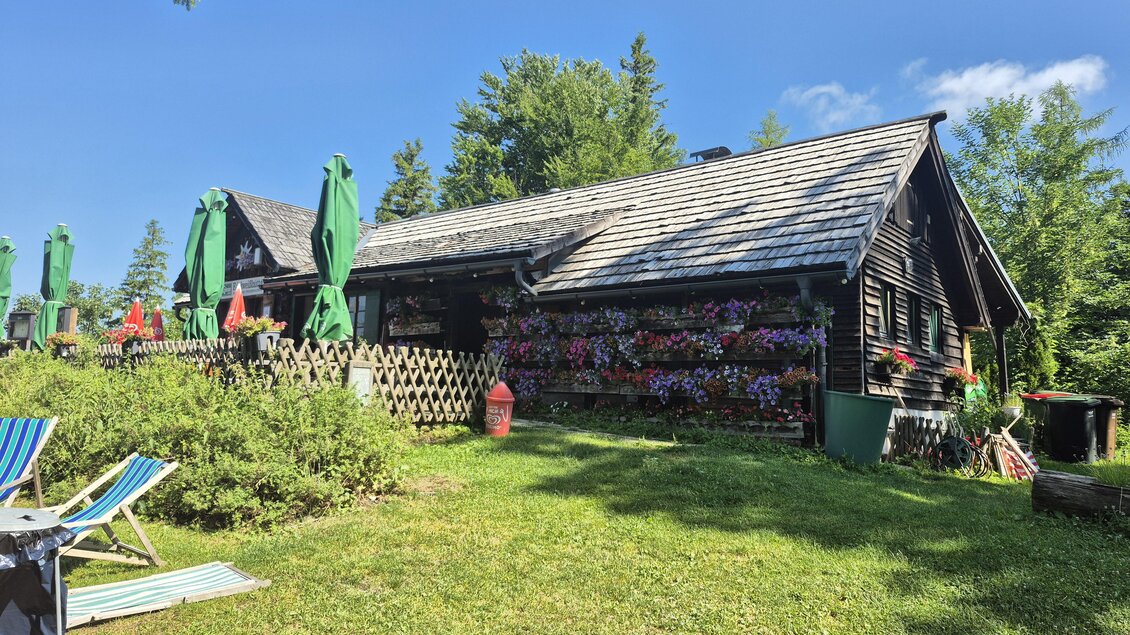Eine gemütliche Hütte umgeben von Blumen und Grün. Sonnenschirme stehen bereit, um Schatten zu spenden.