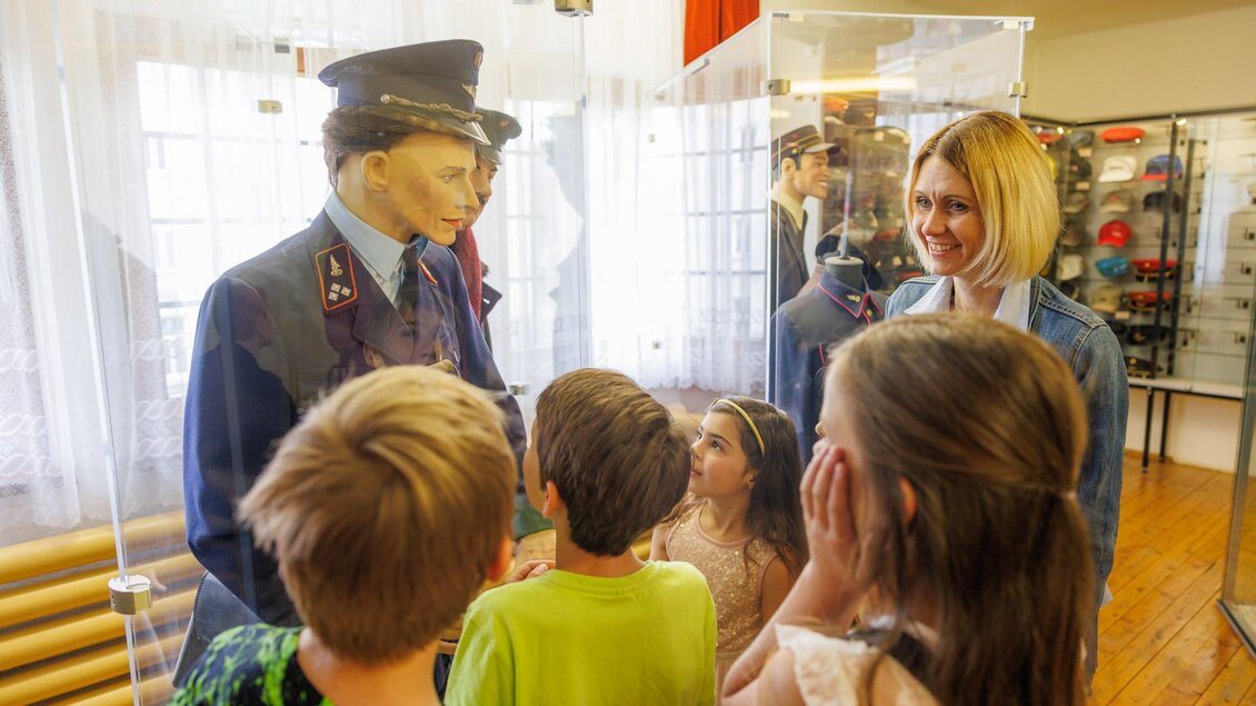 Eine Gruppe von Kindern und einer Frau schaut sich eine Wachsfigur eines Polizisten in einem Museum an. Die Kinder scheinen interessiert und neugierig. | © Erlebnisregion Murtal
