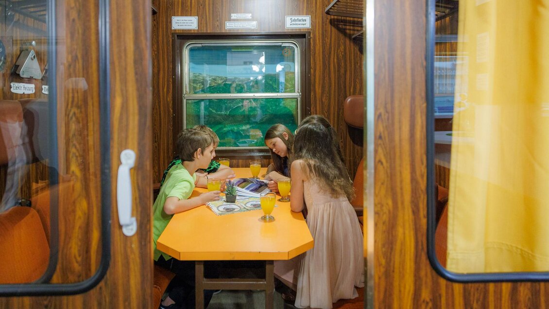 Eine freundliche Gruppe von Kindern sitzt an einem Tisch in einem Zugabteil. Sie genießen Getränke und haben Spaß beim Spielen oder Lesen. | © Erlebnisregion Murtal