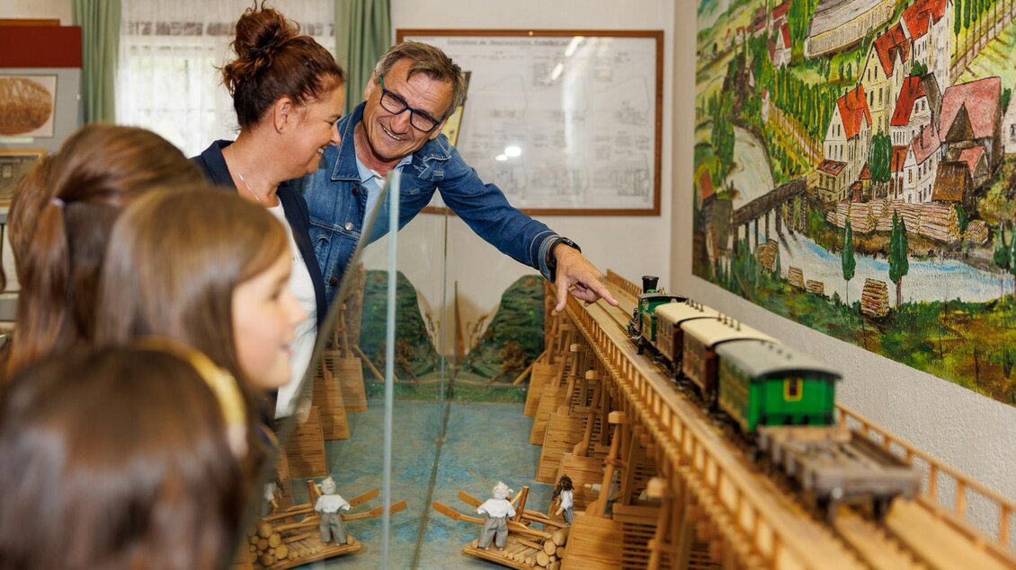 Eine Gruppe von Menschen betrachtet ein Modelleisenbahn-Setup in einem Museum. Sie lächeln und zeigen interessiert auf die Bahn und die Umgebung. | © Erlebnisregion Murtal