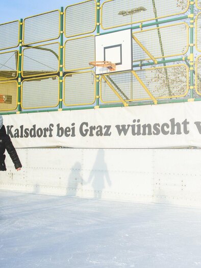 Zwei Kinder skate auf einer Eisfläche. Im Hintergrund ist ein Basketballkorb und ein Banner mit einer Grußbotschaft zu sehen. | © TV Kalsdorf - Mias Photoart1