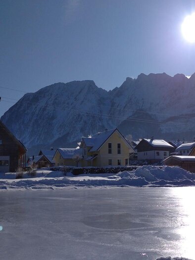 A winter landscape with snow-covered mountains and a frozen pond. The sun shines brightly over the quiet houses. | © Johanna Provatopoulos