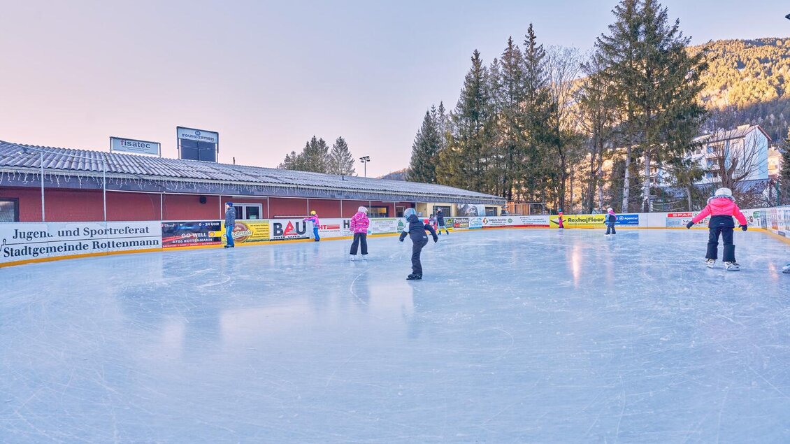 Eine Eisbahn mit mehreren Schlittschuhläufern, umgeben von Bäumen. Die Stimmung ist ruhig und winterlich. | © Thomas Sattler