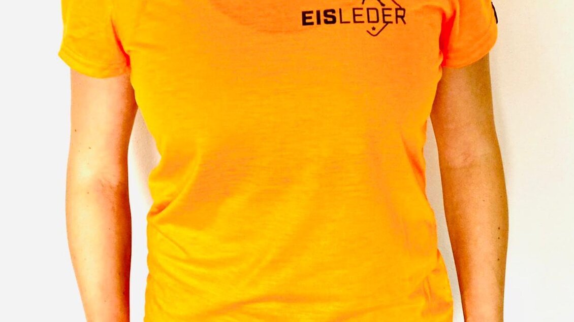 Ein orangefarbenes T-Shirt mit dem Aufdruck "EISLEDER" auf der Brust. Es hat einen runden Ausschnitt und kurze Ärmel. | © Eisleder Bergzeig