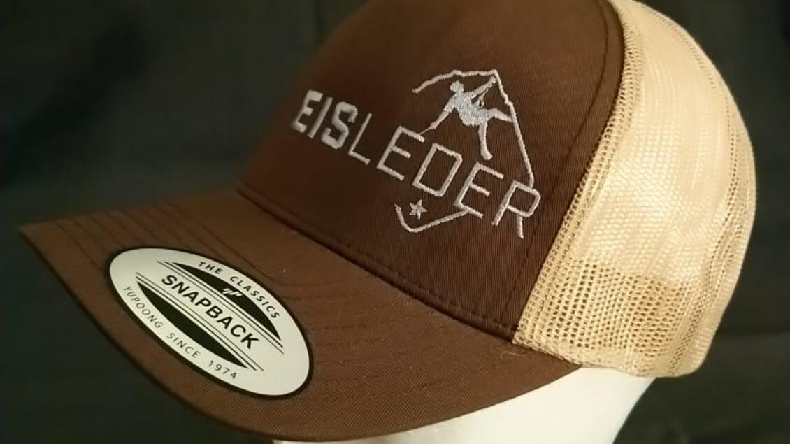 Eine braune Baseballkappe mit einem hellen Netzstoff-Rücken. Das Logo „EISLEDER“ ist sichtbar auf der Vorderseite. | © Eisleder Bergzeig
