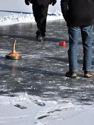 An ice field with several players using curling stones. In the background, footprints in the snow are visible. | © Pixabay