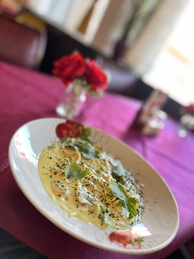 A plate of pasta with a creamy sauce and fresh herbs. In the background, flowers and a set table are visible.