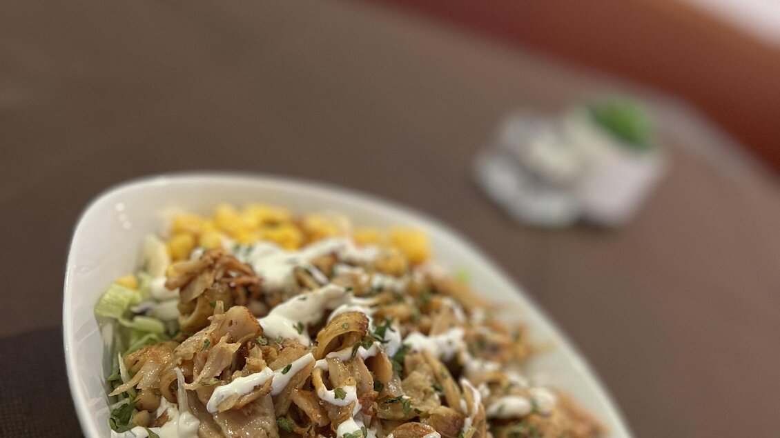 Ein Teller mit Salat, Hähnchenstreifen und einer cremigen Soße. Dazu sind geschnittene Gemüse und eine Beilage aus Reis oder Kartoffeln.