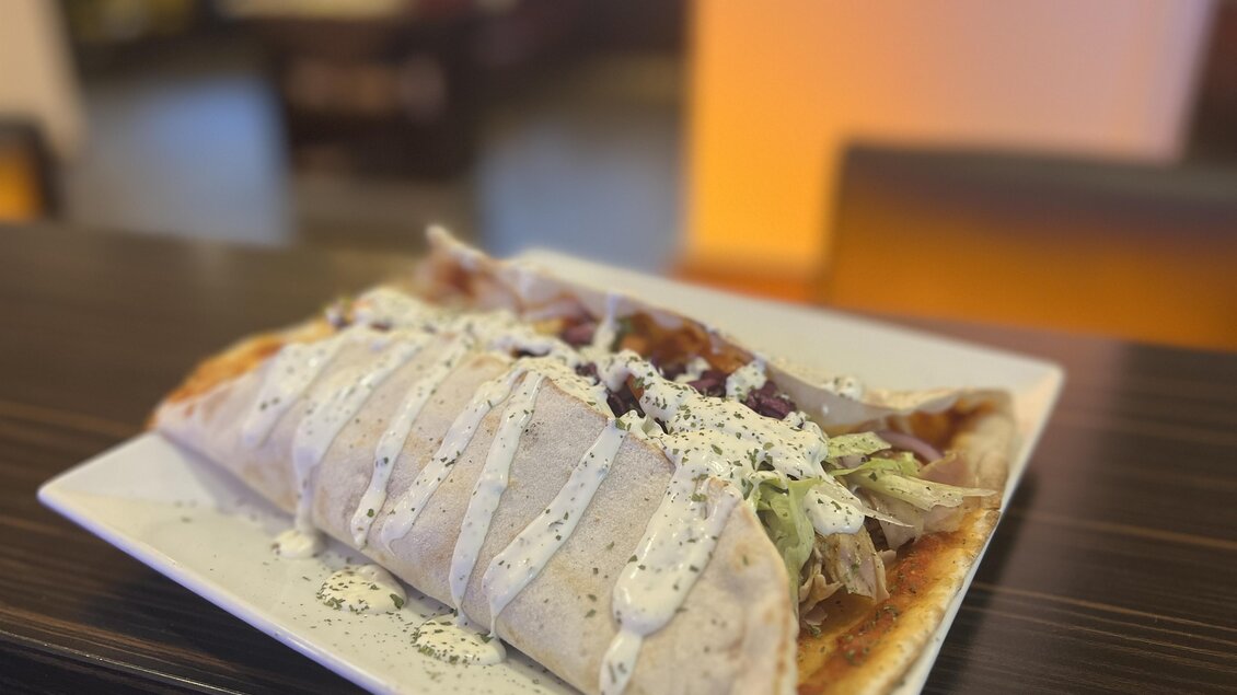 Ein großer Teller mit einem frisch zubereiteten Wrap, gefüllt mit Fleisch und frischem Gemüse. Darüber befindet sich eine köstliche Soße.