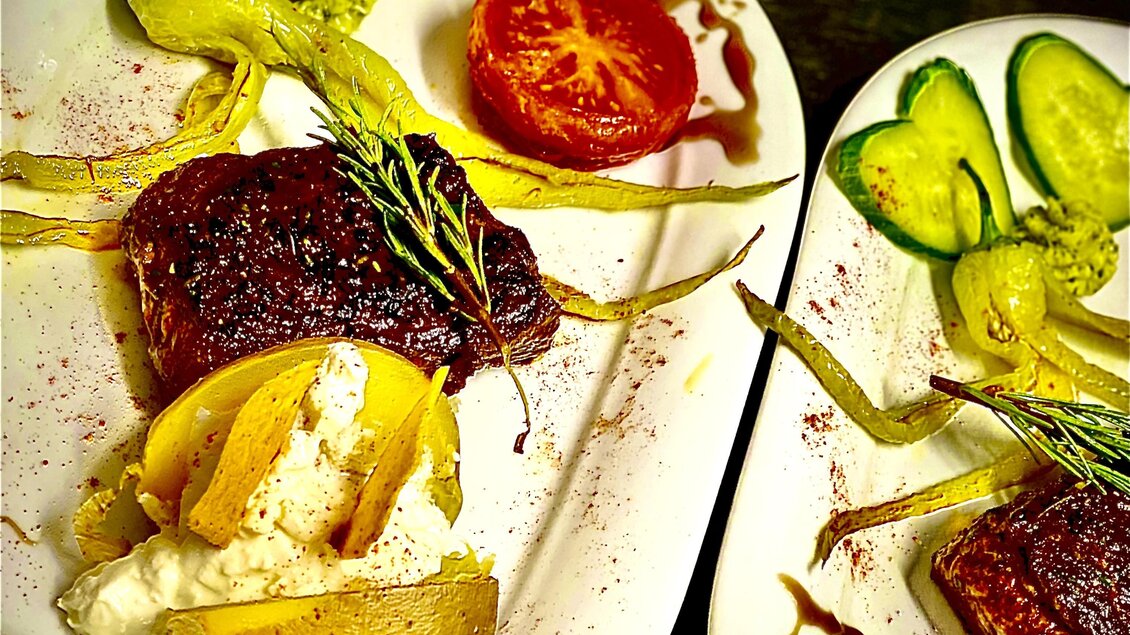 Zwei Teller mit köstlichem Essen, darunter Fleisch, Gemüse und frische Kräuter. Das Gericht ist ansprechend angerichtet mit Tomaten und Gurken.