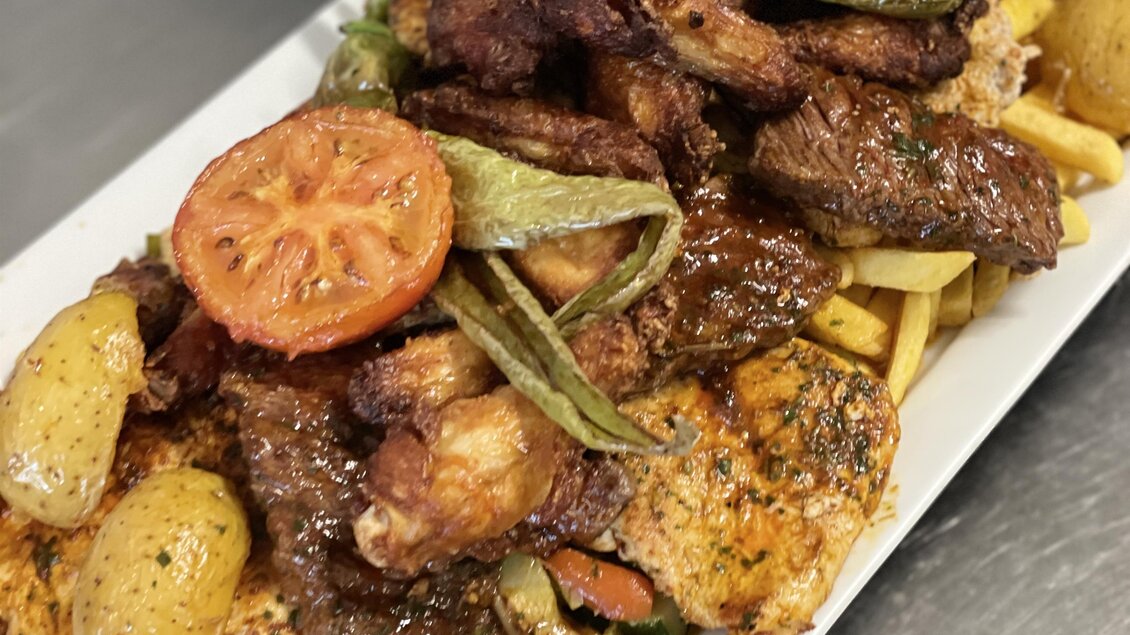 Ein kunstvoll angerichteter Teller mit gegrilltem Fleisch, kleinen Kartoffeln und Gemüse. Das Gericht ist mit gebratenen Tomatenscheiben und grünen Bohnen garniert.