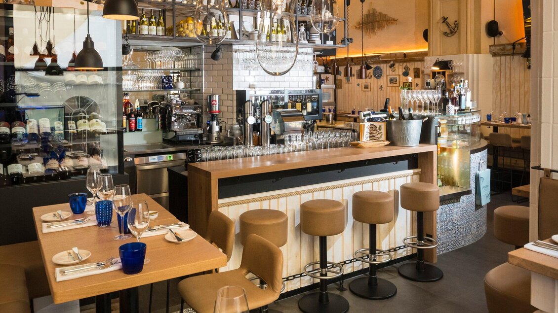 Ein modernes Restaurant mit einer einladenden Bar und stilvollen Holztischen. Die Atmosphäre ist gemütlich und gut beleuchtet. | © El Pescador - Werner Klug