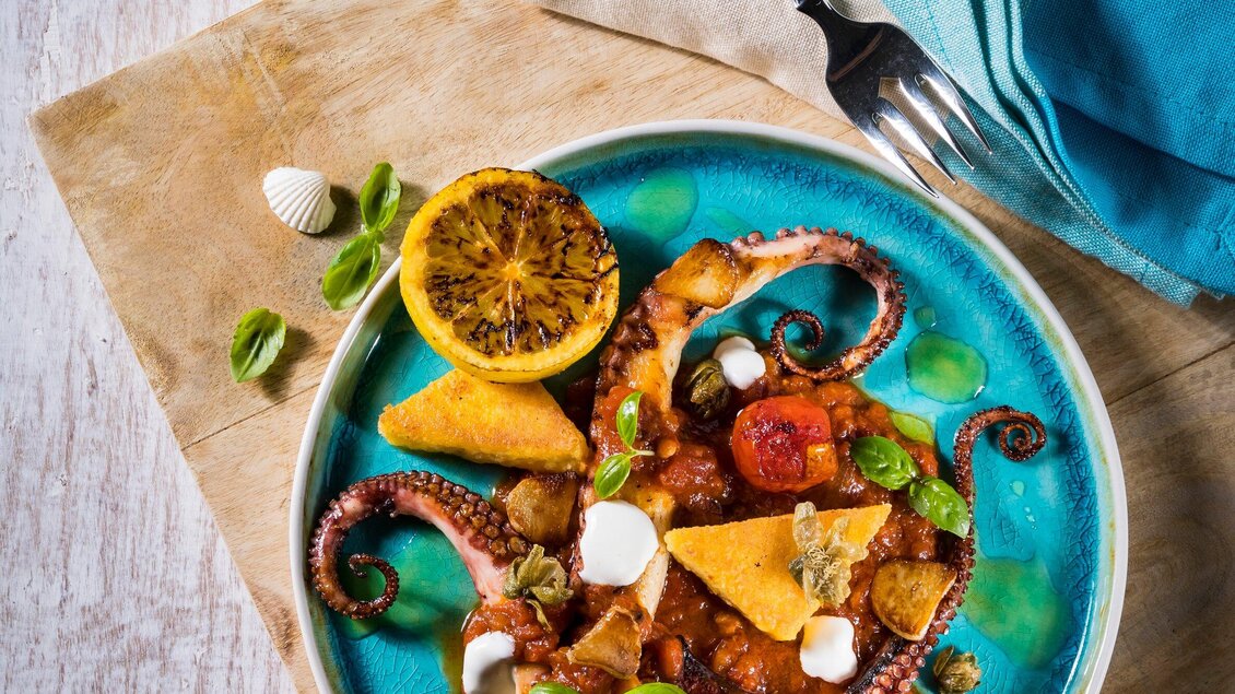 Ein leckerer Teller mit gegrilltem Oktopus, Polenta und buntem Gemüse. Die Anrichtung ist ansprechend und wird durch eine gebratene Zitrone ergänzt. | © El Pescador - Werner Krug