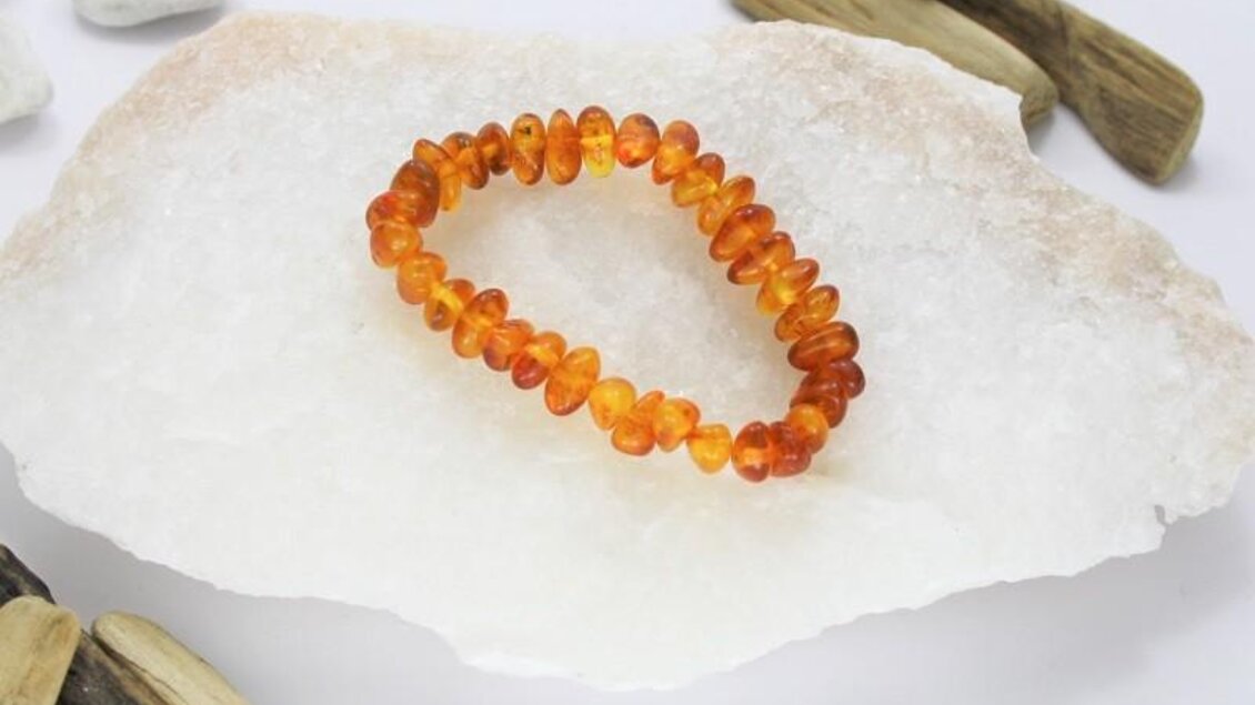 Ein schöner Bernsteinarmreif auf einem mineralischen Untergrund. Umgeben von kleinen Steinen und Holzstücken, strahlt er Wärme und Natürlichkeit aus. | © Elima Schmuck