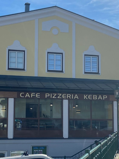 A yellow building with a café, a pizzeria, and a kebab restaurant. The entrance has large windows and there is a terrace. | © TVB Ausseerland_Salzkammergut-Jana Grill