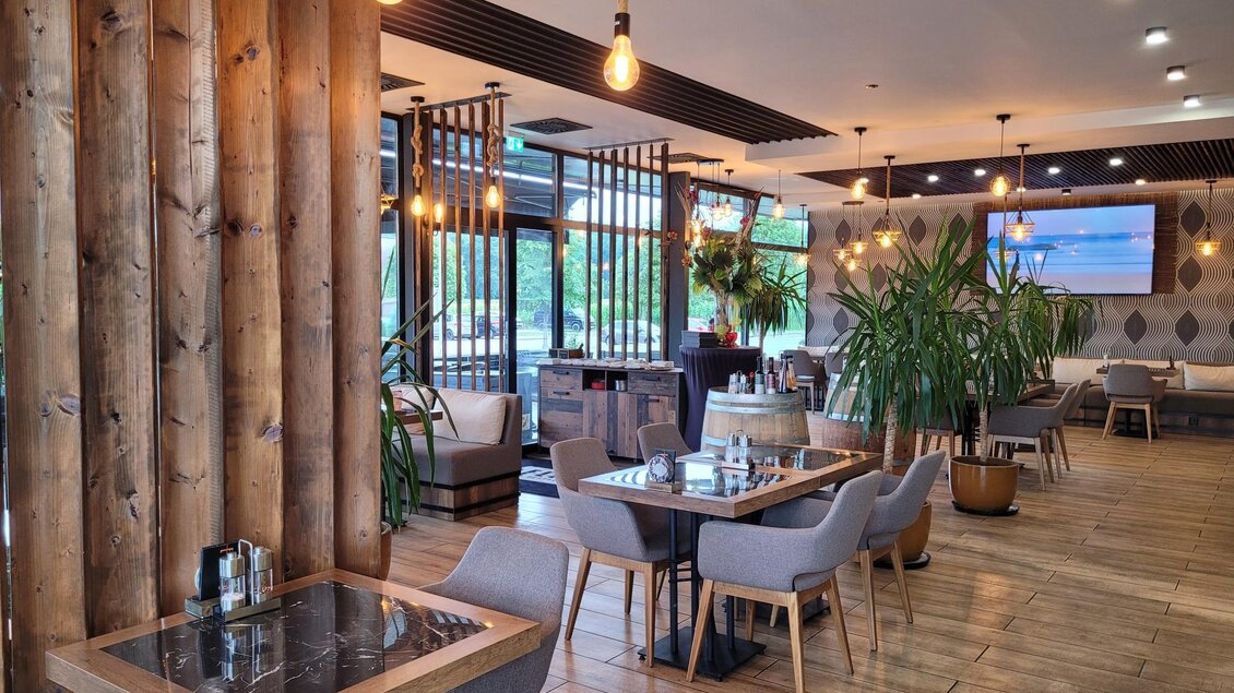 Ein modernes Restaurant mit Holzdetails und gemütlichen Sitzbereichen. Große Fenster lassen viel Licht herein und es sind Pflanzen dekorativ platziert. | © TV Südsteiermark - Irene Löschnig