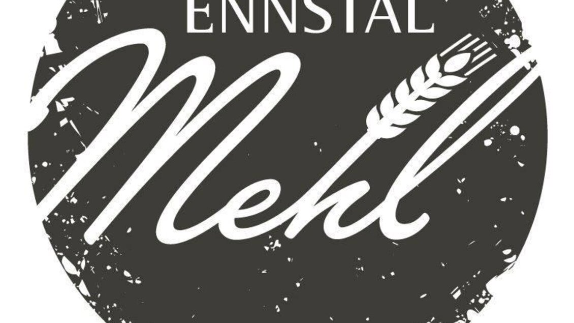 Ein Logo von Ennsta Mehl mit einem stilisierten Weizenähren-Motiv. Der Text „Das Mehl aus der Heimat“ wird unter dem Logo angezeigt.