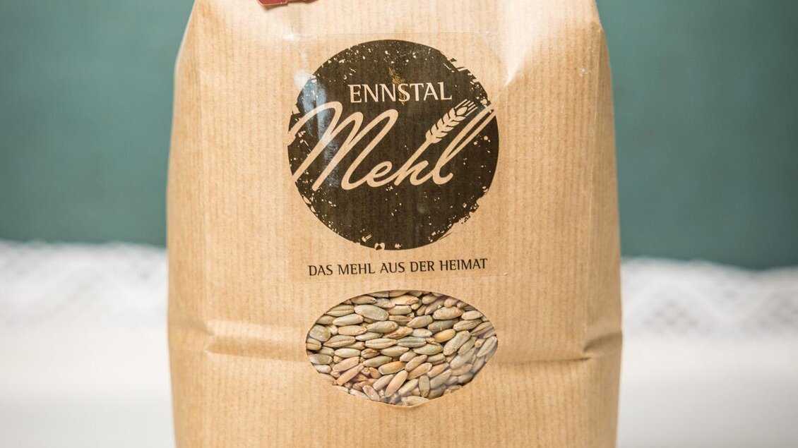 Eine Packung Ennstäler Mehl steht auf einem Tisch. Im Hintergrund sind einige Halme von Weizen zu sehen. | © Netzwerk Kulinarik wildbild