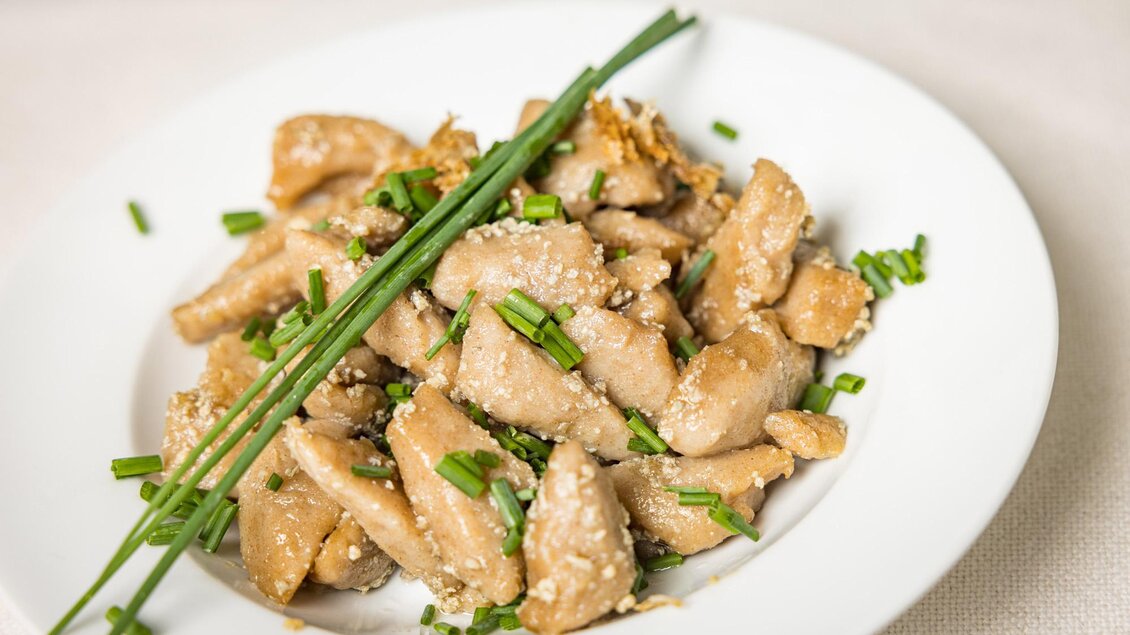 Ein Teller mit zartem Hähnchenfleisch, garniert mit Sesam und Frühlingszwiebeln. Das Gericht sieht appetitlich und frisch aus. | © Netzwerk Kulinarik wildbild