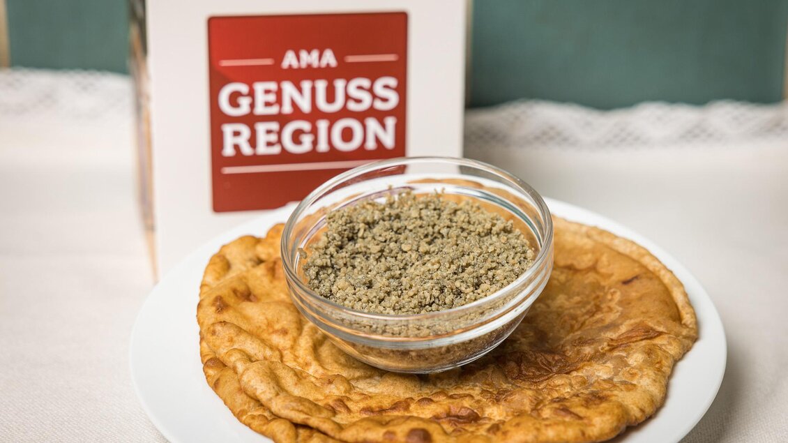 Eine Portion flache Pfannkuchen liegt auf einem Teller, daneben befindet sich eine Schale mit einer Gewürzmischung. Im Hintergrund steht eine Box mit der Aufschrift "AMA GENUSS REGION". | © Netzwerk Kulinarik wildbild