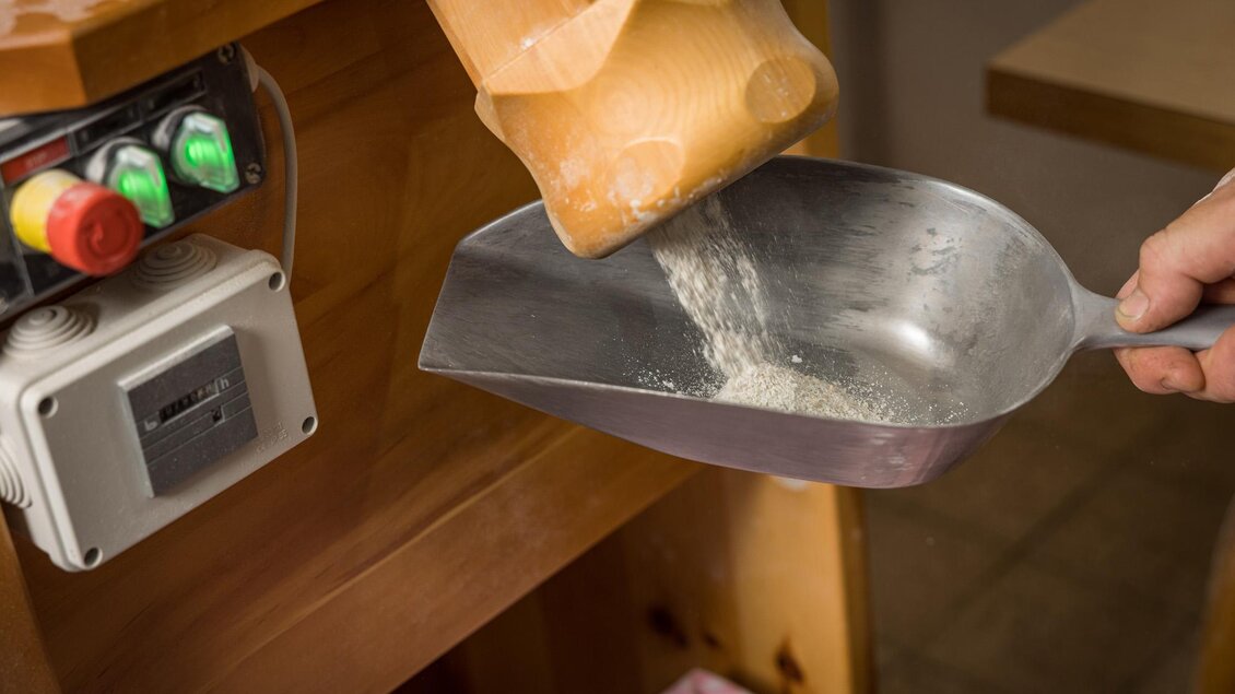 Ein Handgriff mit einer Schaufel, die Mehl aus einem Behälter aufnimmt. Im Hintergrund sind eine Holzoberfläche und einige Bedienelemente sichtbar. | © Netzwerk Kulinarik wildbild