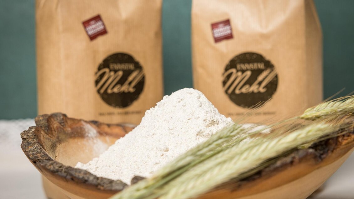 Ein Holzschüssel mit frischem Mehl und Ähren. Im Hintergrund stehen zwei Tüten Mehl. | © Netzwerk Kulinarik wildbild