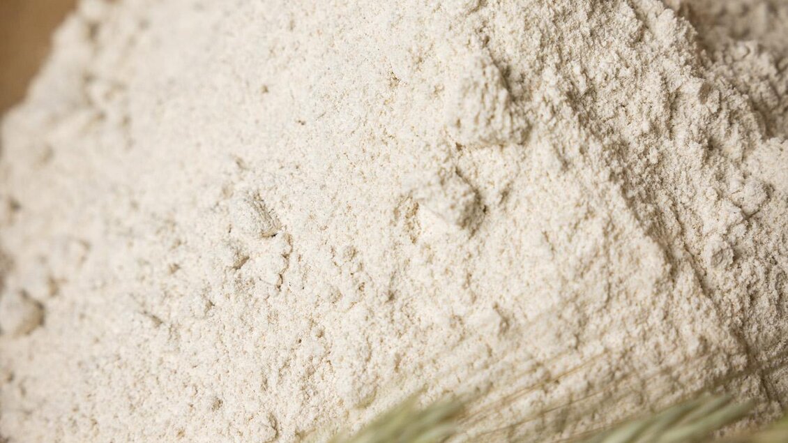 Ein Haufen Mehl in einer Holzschale, umgeben von Ähren. Die Textur des Mehls sieht fein und frisch aus. | © Netzwerk Kulinarik wildbild